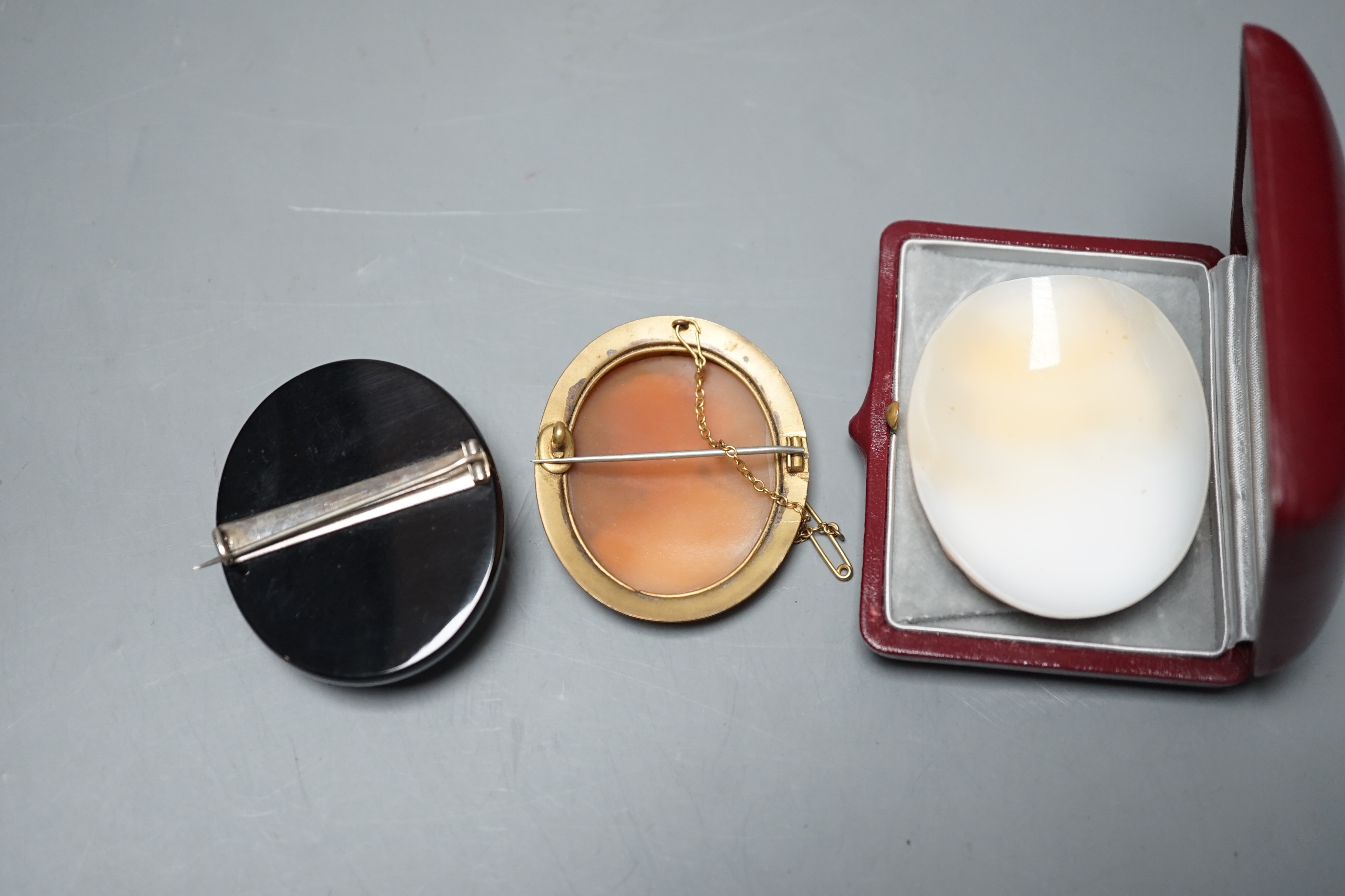 A good quality unmounted oval cameo shell, carved with the bust of a Roman soldier to sinister, 56mm, in Antrobus box, together with two cameo set brooches.
